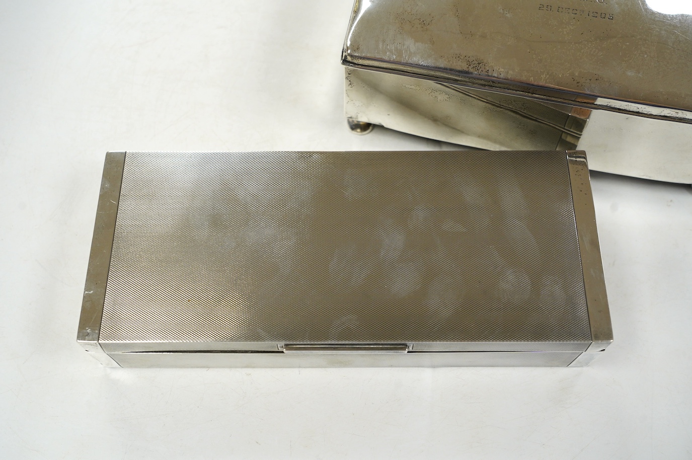 A George V engine turned silver cigarette box, by Padgett & Braham Ltd, London, 1935, 21.6cm and an earlier Irish silver cigarette box. Condition - poor to fair